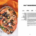 Seafood paella in a skillet with mussels and shrimp on an orange cloth, next to a German recipe page titled 'Pilaf mit Meeresfrüchten'.